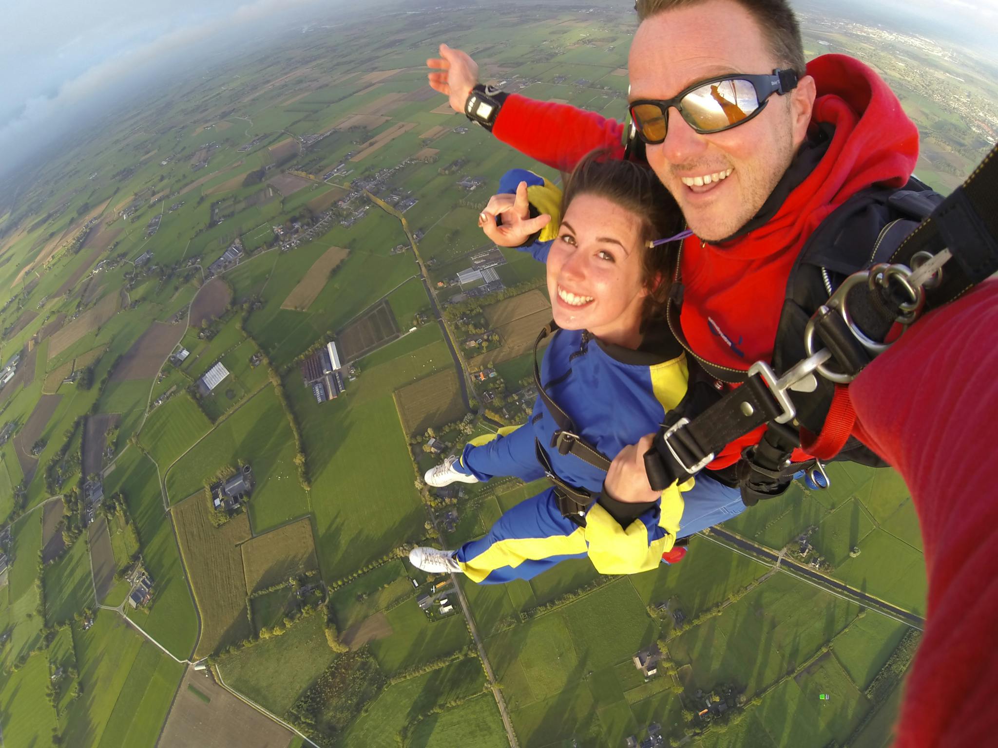 A thrilling tandem skydive experience captured with a panoramic view of lush farmland below.
