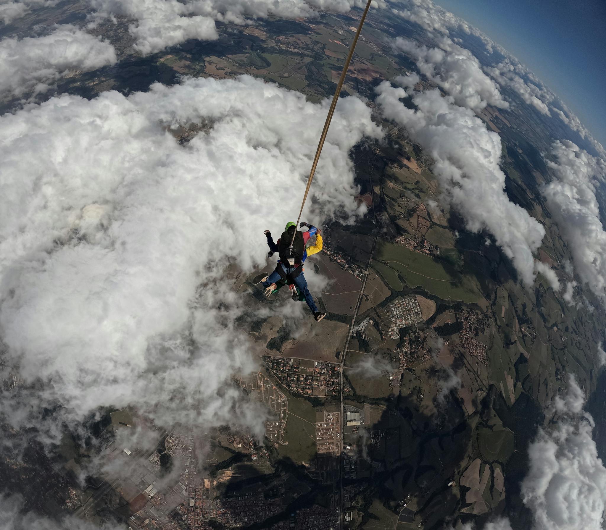 Tandem skydivers bravely descend through clouds with a parachute, capturing aerial views.